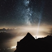 man on mountain shooting flashlight at stars at night